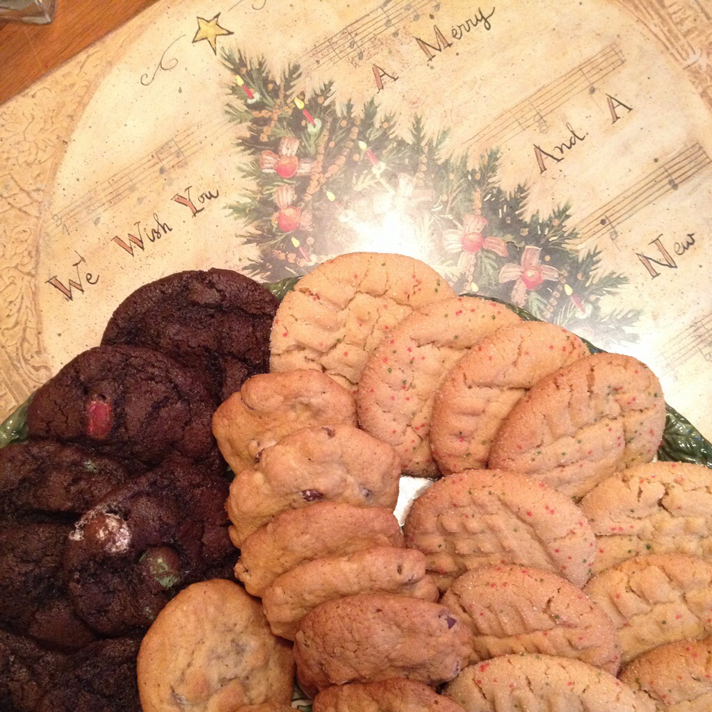 Three kinds of cookies — chocolate with m and m's, chocolate chip, and peanut butter — sit on a christmas placemat.